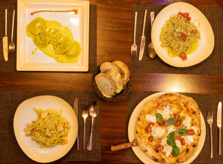 Pizza aus dem Steinofen neben Ravioli und Pasta, von oben fotografiert