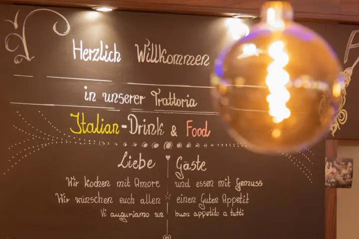 Kreidetafel mit dem Gruß Herzlich Willkommen in unserer Trattoria